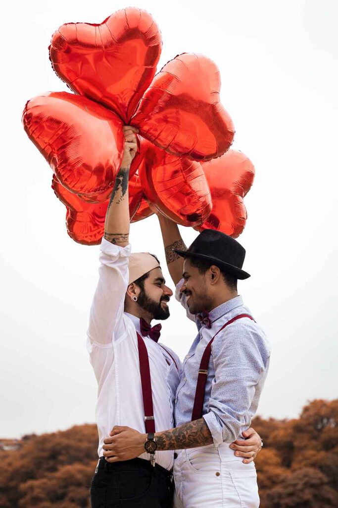 coppia di gay innamorati che si abbracciano con in mano palloncini rossi a forma di cuore